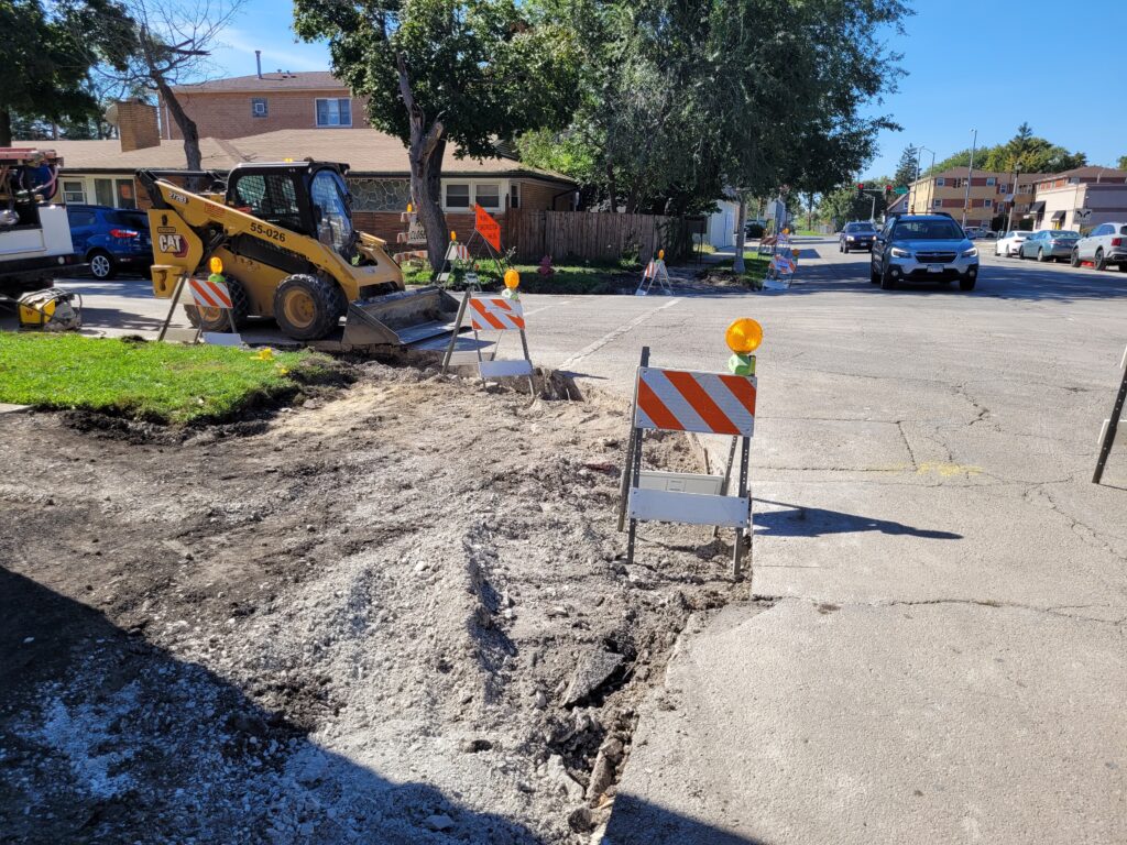 Aggregate base at a sidewalk corner along 16th Street, with construction equipment and barricades nearby.