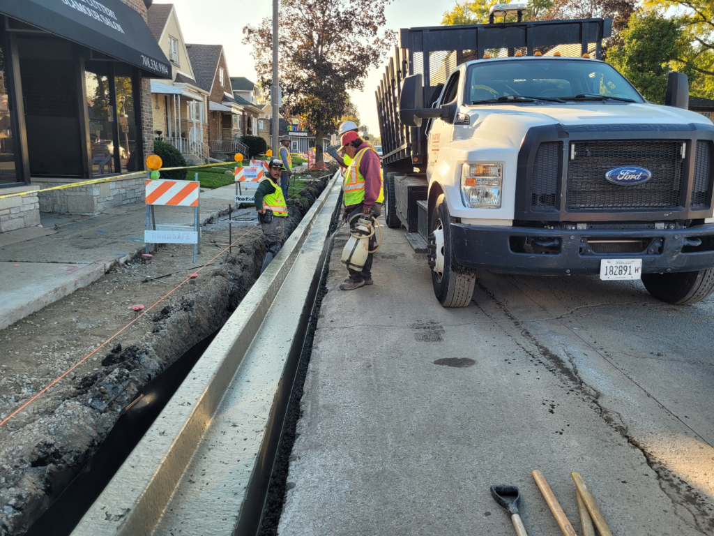 Crew placing concrete curb and gutter along 16th Street beside a concrete truck.